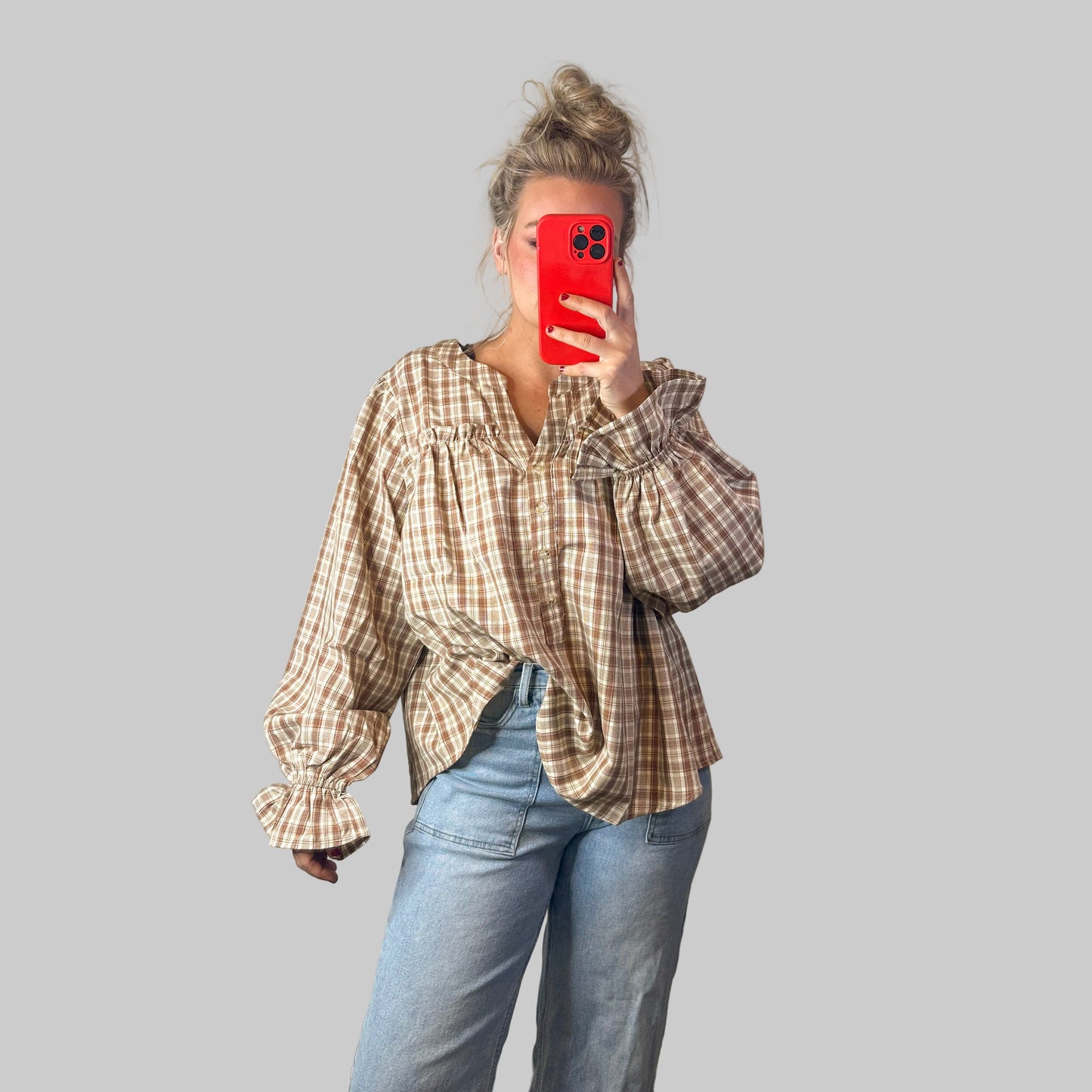 Person wearing a plaid shirt and jeans, holding a red phone with a white wall background