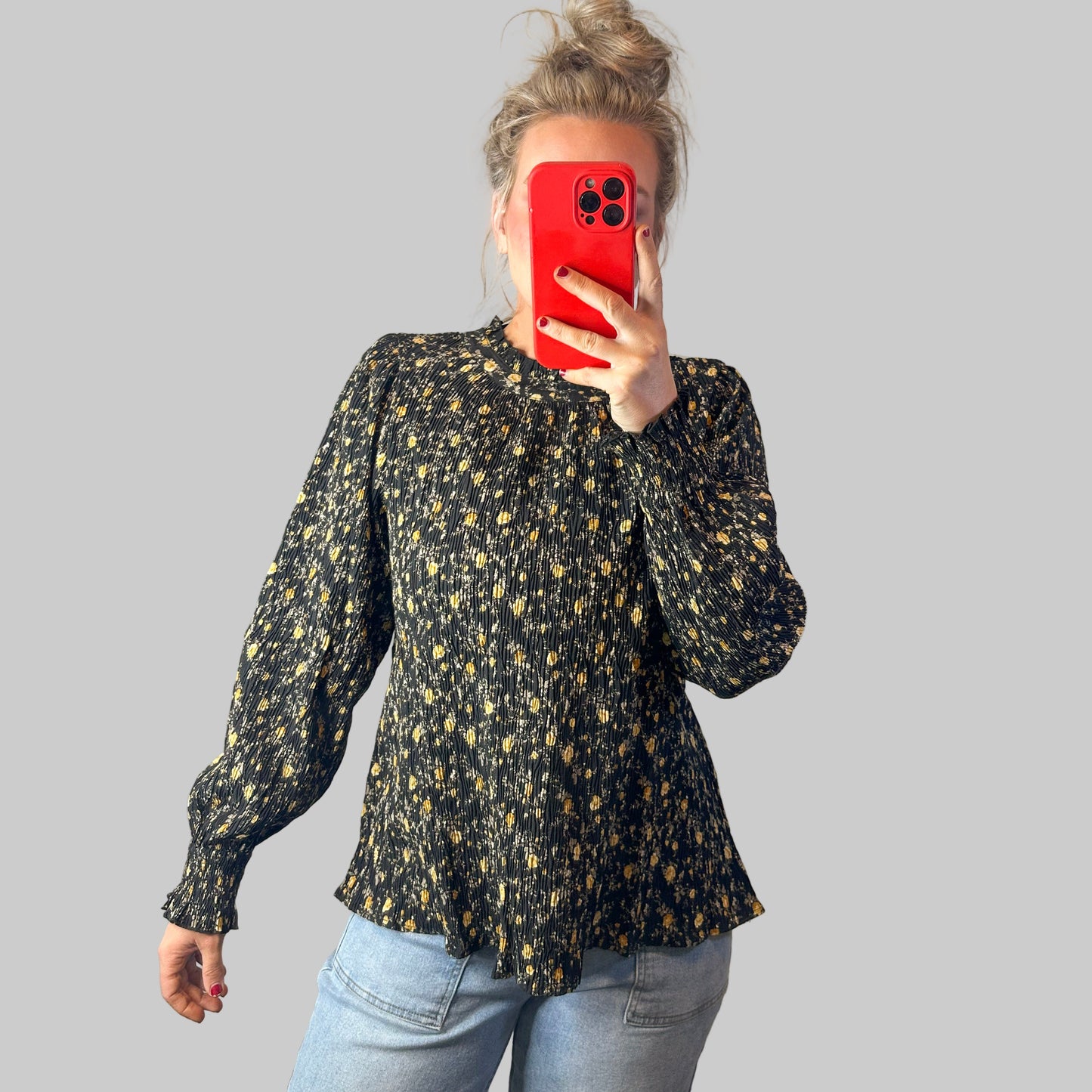 Person wearing a black floral blouse and blue jeans taking a mirror selfie.